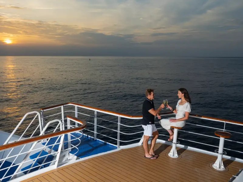 A couple sharing a toast on the Sun Deck of La Pinta at sunset