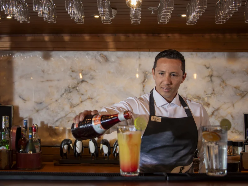 A bartender preparing a cocktail at the Panorama Lounge Bar aboard Galápagos Legend
